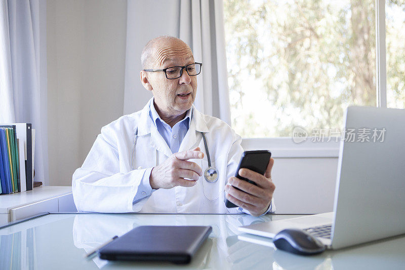 高级男子医生与病人使用智能手机远程医疗预约。