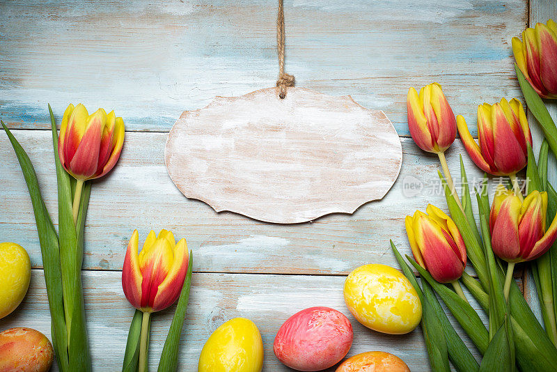 复活节彩蛋用混合颜色的郁金香排列在木桌上平铺顶视图