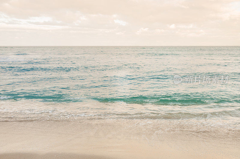 柔和的日落天空在蓝绿色的海浪横扫棕榈滩的海岸线，佛罗里达
