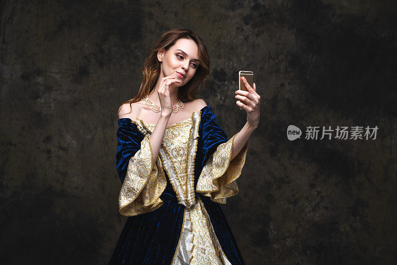 美丽的女人穿着文艺复兴时期的服装，用智能手机自拍，新旧概念