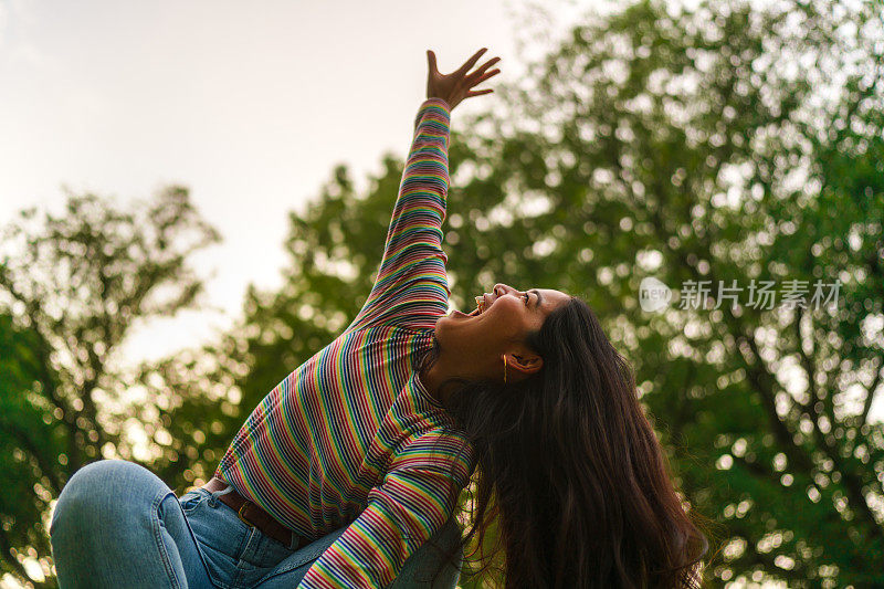 在大自然中，快乐的年轻女子举起她的手向天空的肖像