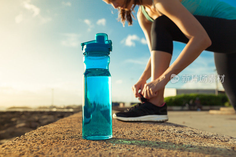 女跑步者系着她的鞋子旁边的一瓶水
