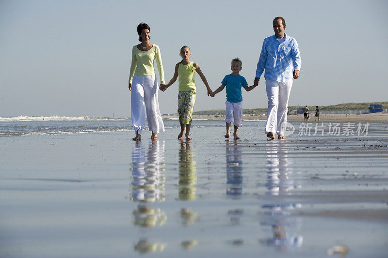 幸福的四口之家穿着鲜艳的衣服沿着海滩散步