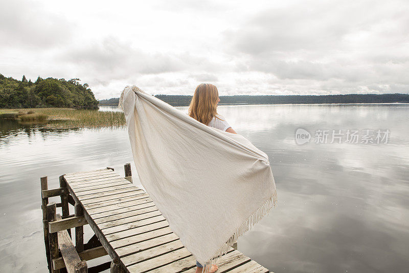 女人站在湖码头上，拿着毯子在空中