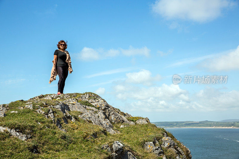 一个成熟的西班牙女人站在遥远的海岸岬角上