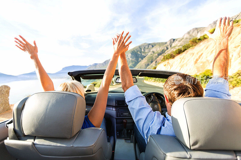 在公路旅行期间在车里举起手臂的幸福夫妇