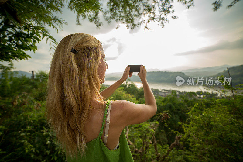 年轻女子在山顶用手机拍照