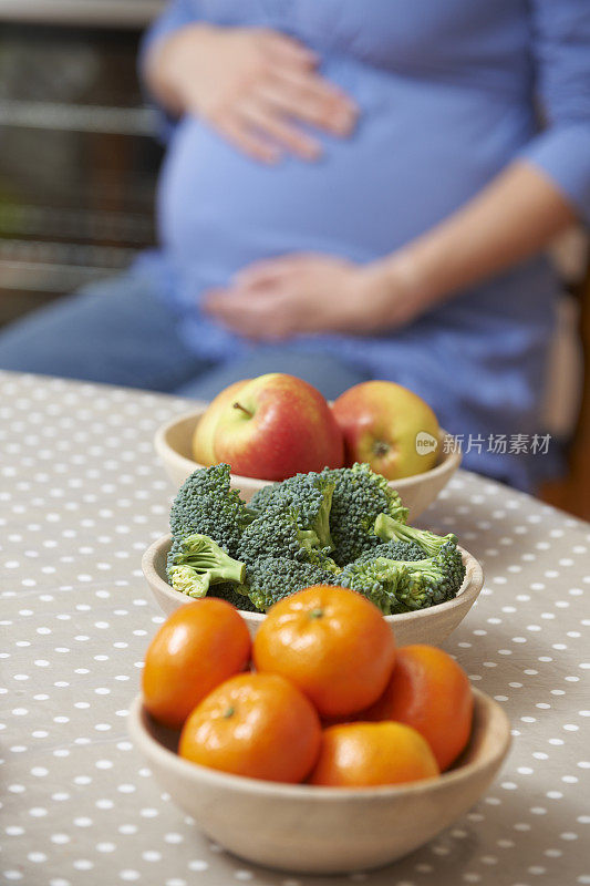 孕妇看着一碗健康的水果和蔬菜
