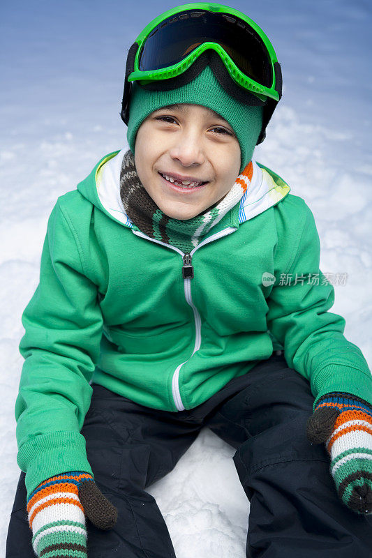 微笑的男孩坐在雪地上滑雪