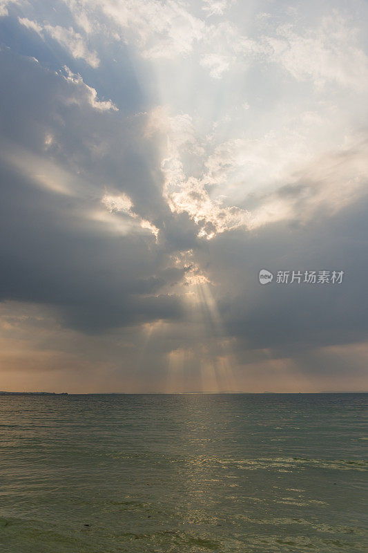在平静的热带海面上，阳光透过云层射出上帝的光芒。
