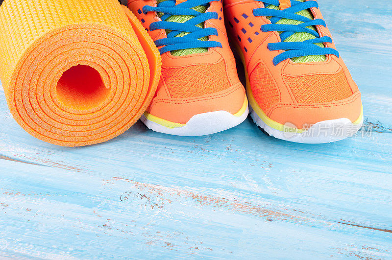 运动器材和运动鞋。瑜伽垫和运动鞋上的蓝色木制背景。健康的生活方式，健康的食品，运动和饮食的概念。本空间