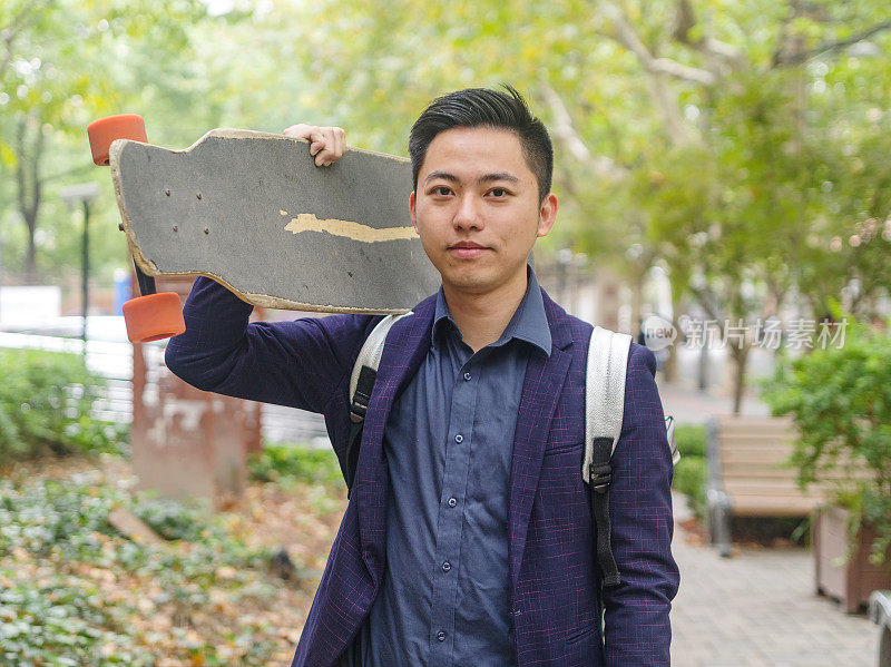 这是一幅英俊的中国年轻人的肖像，他把滑板扛在肩上，对着镜头微笑。