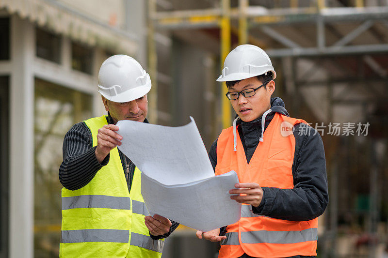 年轻的亚洲学徒在建筑工地与资深工程师工作。在户外
