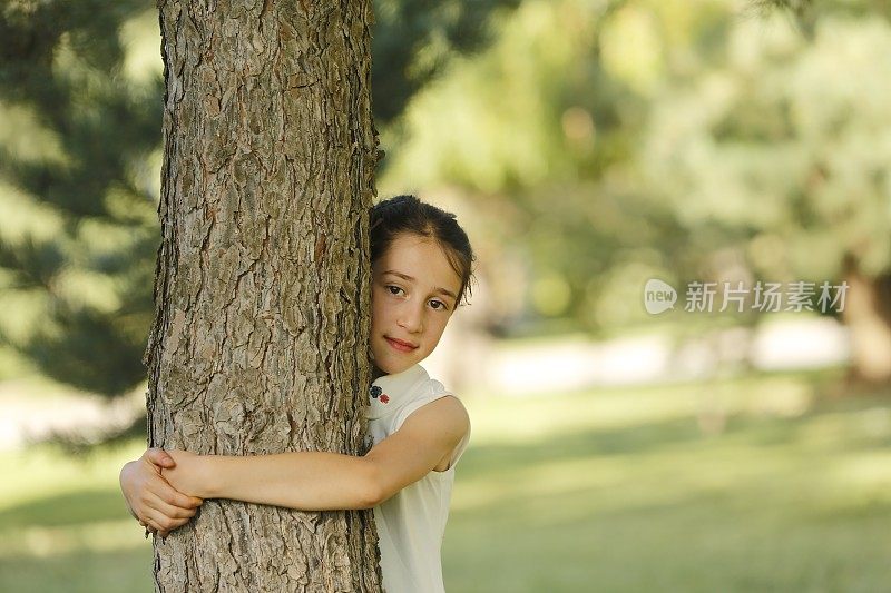 美丽的小女孩微笑着拥抱着树干