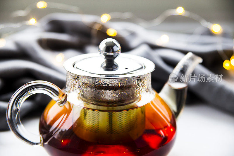 一个红茶茶壶，旁边放着一条灰色围巾和圣诞花环。冬天的概念