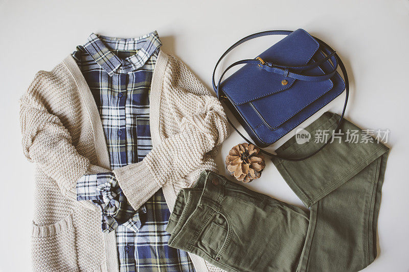 秋女人休闲时尚套平lay。格子衬衫，针织毛衣，蓝色斜挎包和卡其布裤子在白色背景。时髦的服装俯视图。