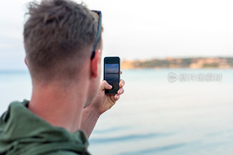 年轻的成年男子用手机拍摄大海