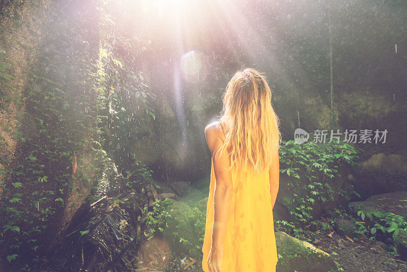 一个女孩站在热带雨林的洞穴里，仰望着从岩石上射下来的壮丽的阳光。人们旅行的奇妙欲望自然的概念