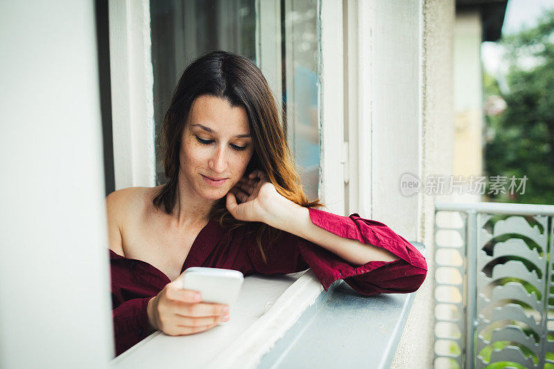 穿着红色衣服的女孩在窗户边拿着手机