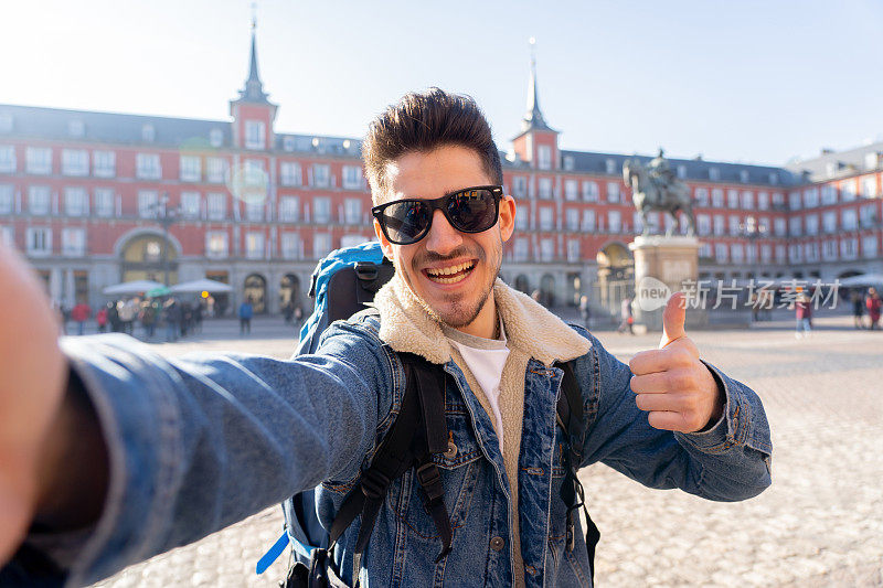 有吸引力的年轻旅游学生男子背包有乐趣，快乐和兴奋与智能手机微笑自拍广场，西班牙马德里市长。度假、环游世界的概念。