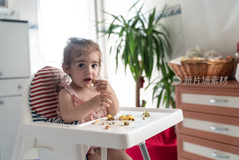 蹒跚学步的小女孩坐在喂食椅上吃食物