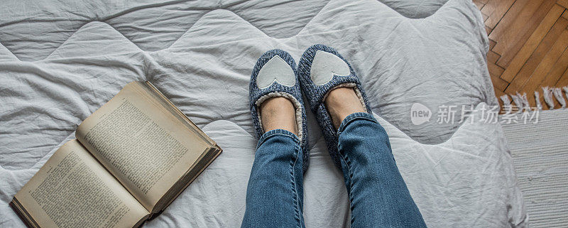 个人观点女人的腿放松在床上穿着蓝色拖鞋