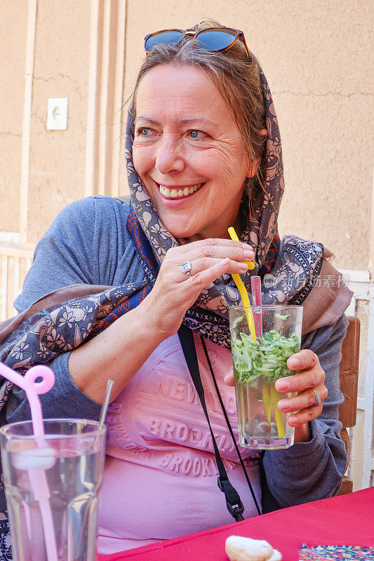 微笑的成熟女人在伊朗旅行时喝玫瑰水和黄瓜