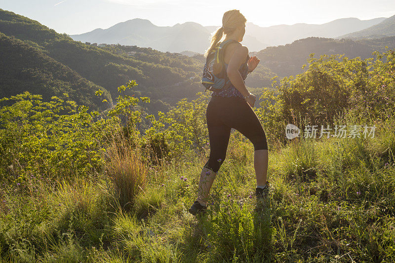 日出时，女跑步者穿过长满草的山脊