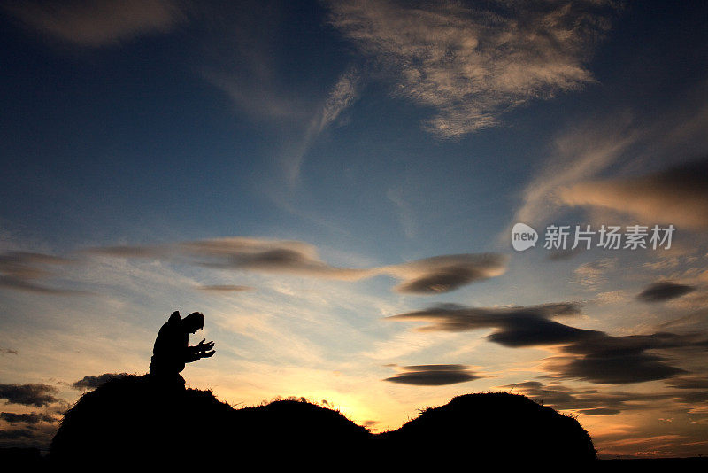 在美丽的日落天空下祈祷的人的剪影