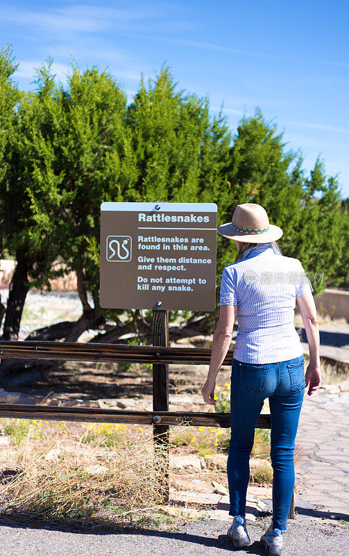 一名女子在自然公园阅读响尾蛇警告标志