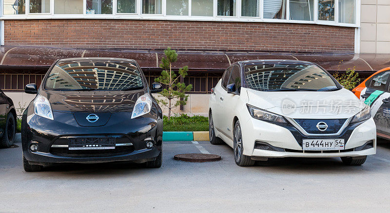 两辆日本产的日产聆风电动车停在一座多层建筑附近的柏油路上。环保的交通工具。