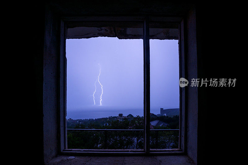透过一间废弃房屋的窗户，可以看到黑海上空的雷雨