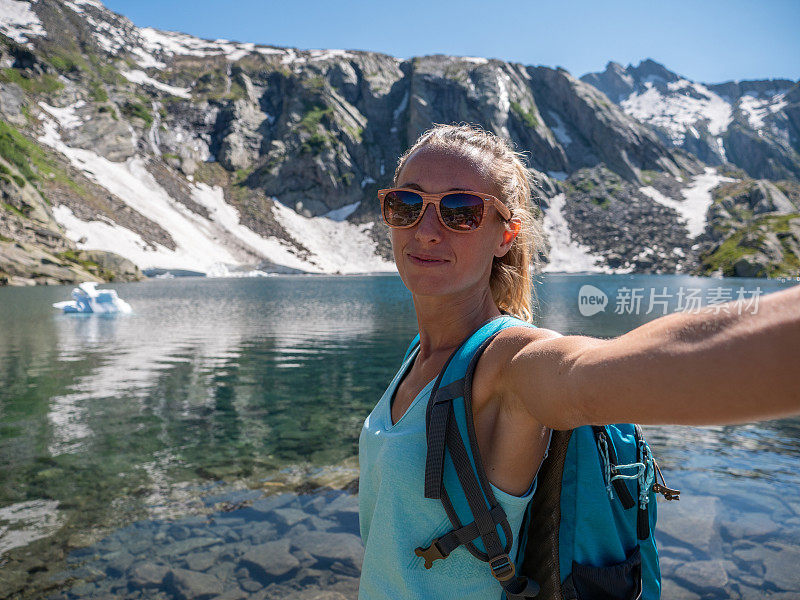 年轻女子在美丽的高山湖周围徒步旅行时自拍