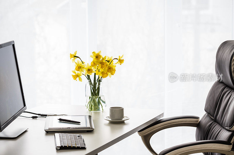一个小的办公室办公桌的安排与一束水仙花的颜色流行