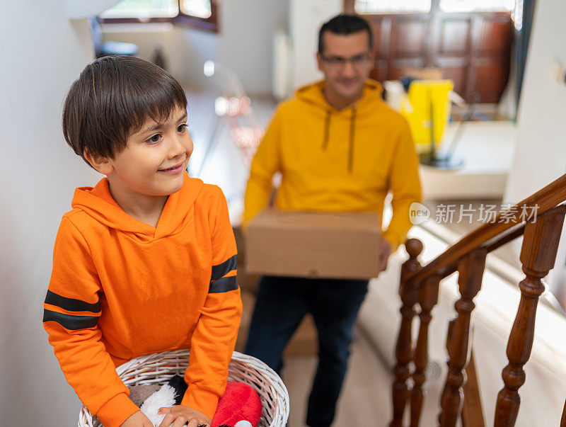 一个可爱的快乐的男孩和他的父亲正在搬运箱子楼梯搬家到新家。