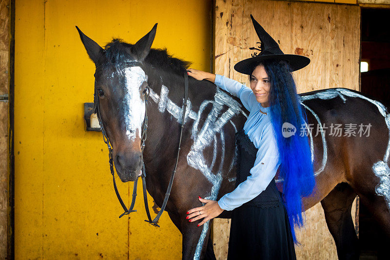一个打扮成女巫的女孩站在一匹马旁边，马上有一具用白漆涂着的骷髅