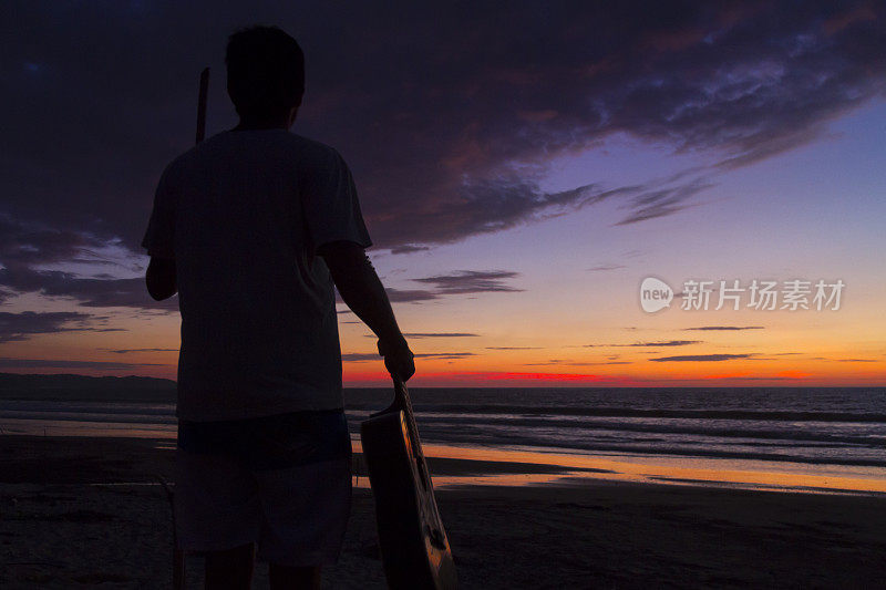 一个拉丁健康肌肉男子冲浪者站在海边与原声吉他在日落时间，放松在卡诺阿，Manabi省，厄瓜多尔，拉丁美洲