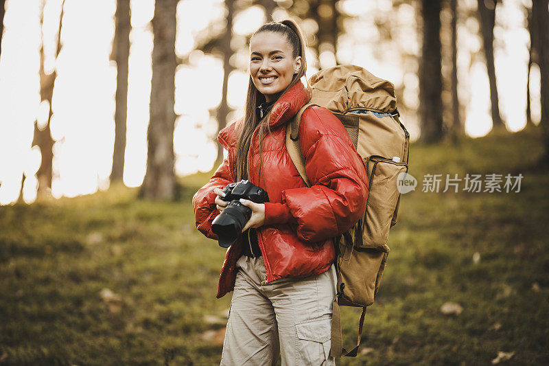 年轻的徒步旅行者与相机在自然界的肖像。成功的女人徒步登山在日出的山顶-年轻的女人背包上升到山顶。发现旅游目的地