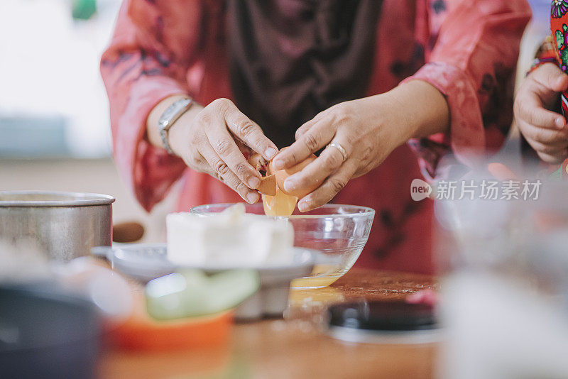 马来西亚母亲打破鸡蛋，展示她患有唐氏综合症的女儿在厨房做传统马来甜点