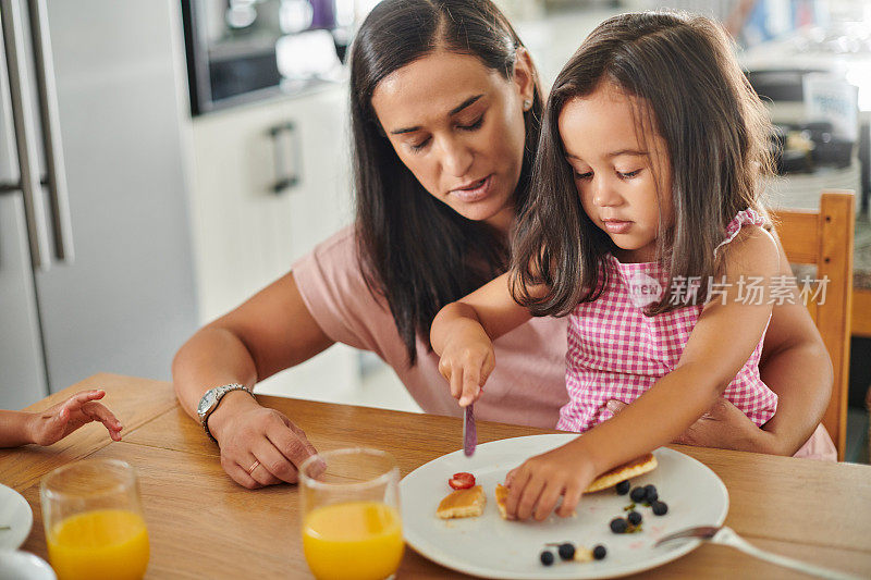 一个可爱的小女孩和她的妈妈在家里吃煎饼当早餐