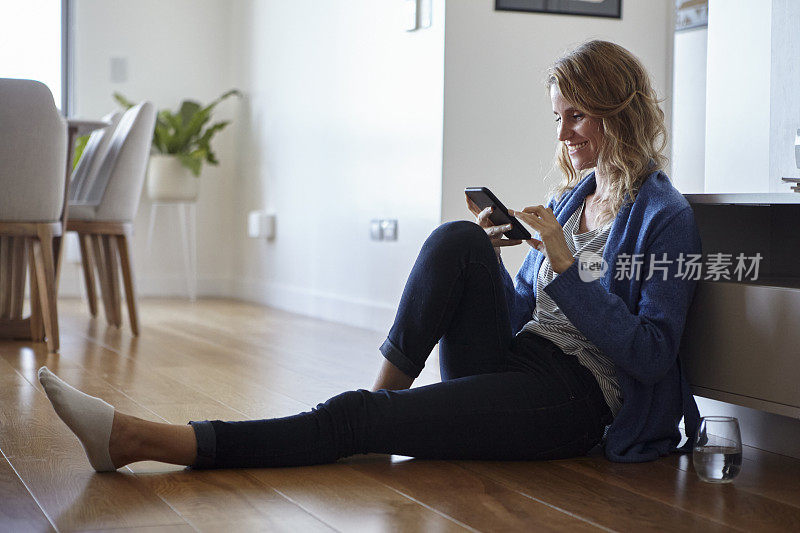 微笑的中年妇女的肖像，当靠在沙发上或坐在家里的地板上发短信