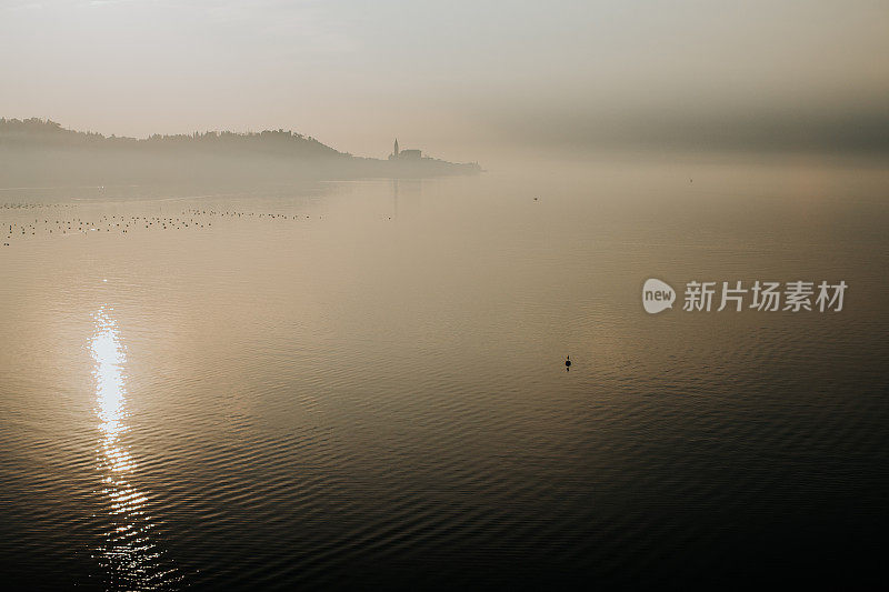 太阳反射在雾蒙蒙的海面上，教堂在海角的距离