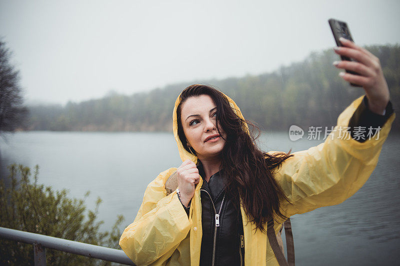 一个快乐的年轻女子在一个下雨天穿着一件黄色雨衣在树林里享受大自然。