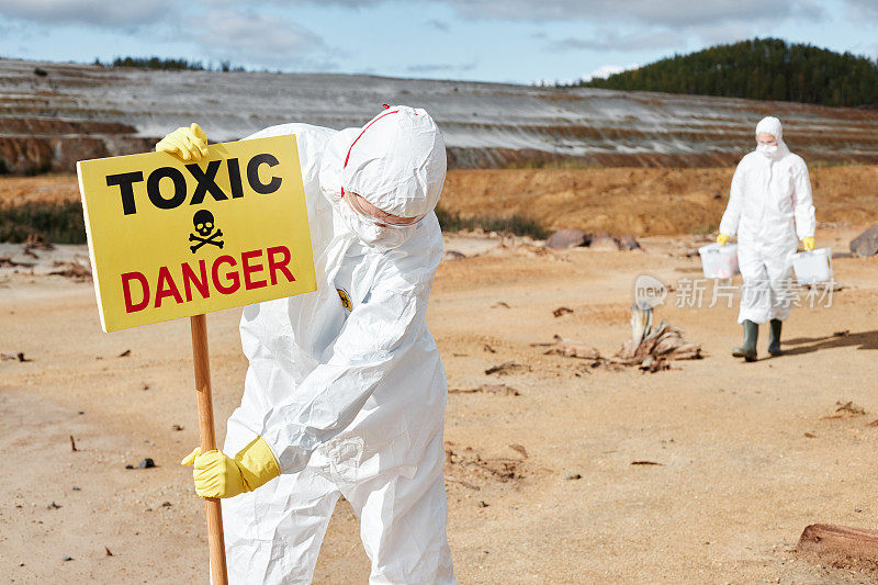 环境灾难后，穿着防护服的生态科学家在荒地上安装有有毒危险文字的标志
