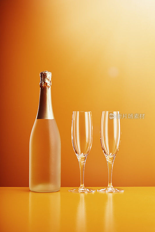 橙色背景下的香槟酒瓶和玻璃杯