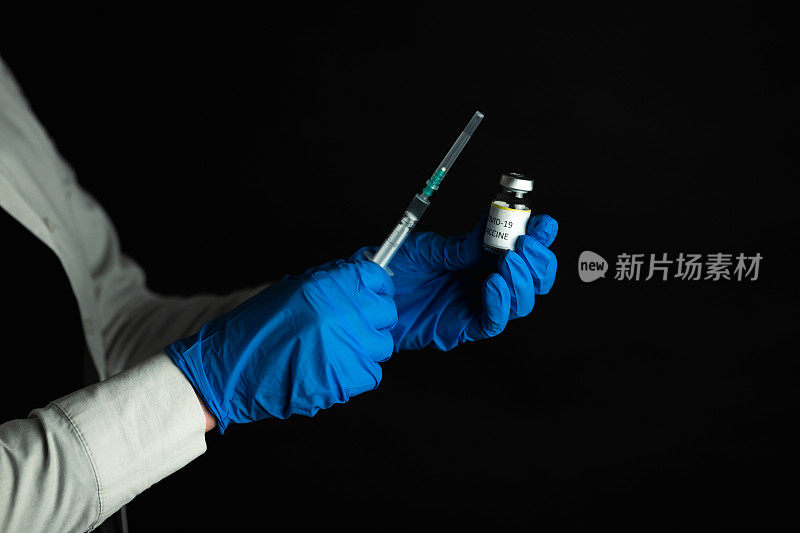 戴着乳胶手套的护士，手里拿着COVID-19疫苗瓶和注射器
