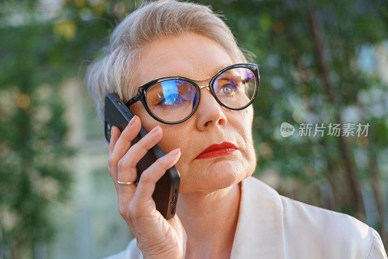 这是一位精心打扮的老妇人的特写镜头，她在看向别处，打着电话