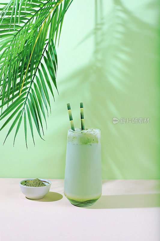 绿茶抹茶拿铁在玻璃与竹管在现代浅色背景与棕榈叶。传统的印度饮料富含抗氧化剂