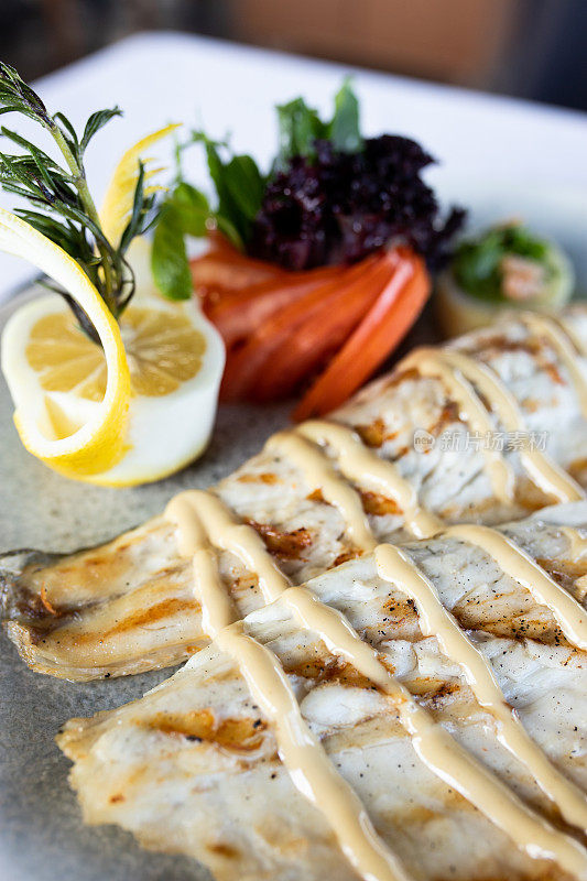 白色盘子上烤海鲈鱼配番茄和柠檬