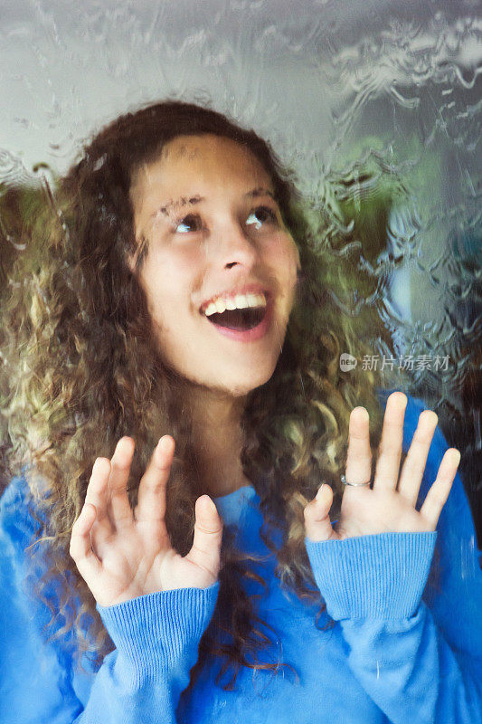 快乐、美丽的年轻女子从被倾盆大雨淋湿的窗口望出去
